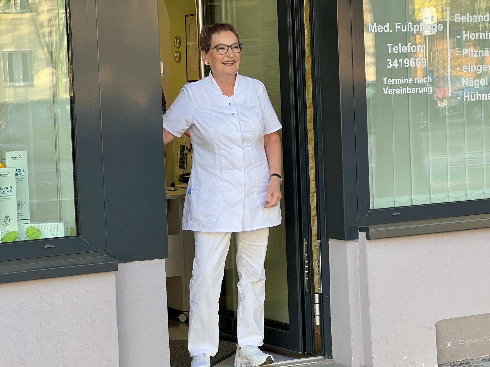 Gabriele Blanke, Podologin, im weißen Kittel im Eingang ihrer Praxis in Berlin-Charlottenburg